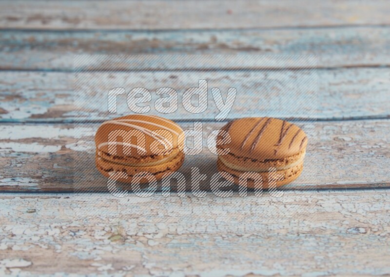 45º Shot of of two assorted Brown Irish Cream, and light brown Almond Cream macarons next to each other on light blue background