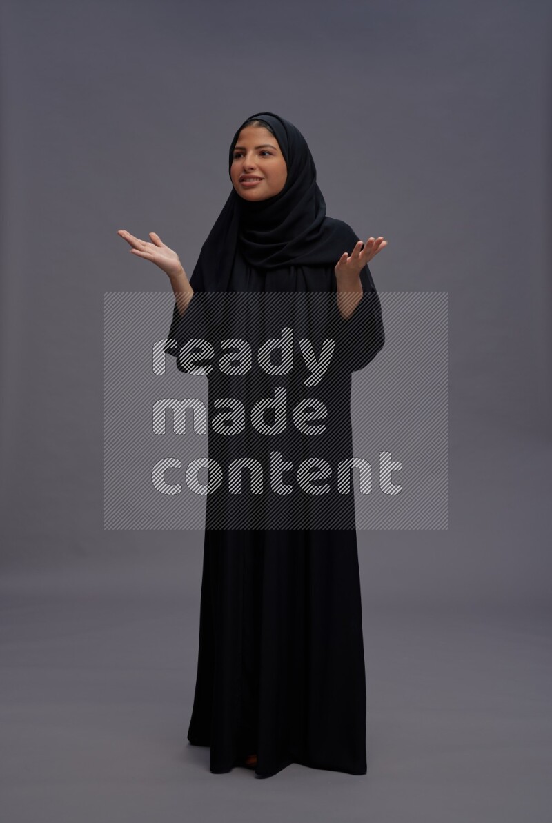 Saudi woman wearing Abaya standing interacting with the camera on gray background