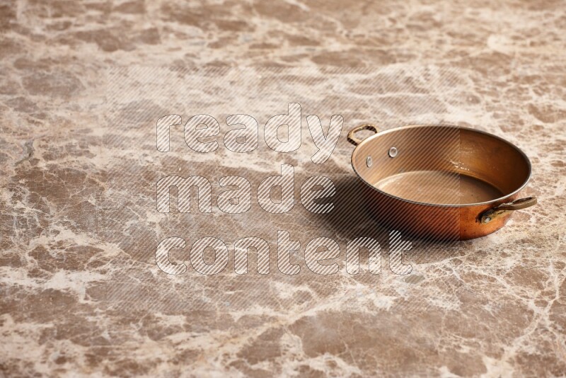 A small copper pan on beige marble background