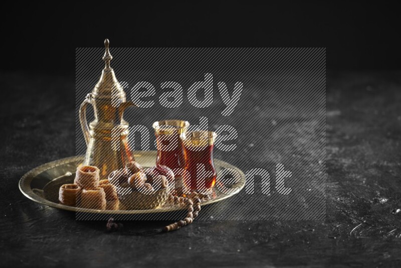 Oriental sweets with dates and a drink on a metal tray in a dark setup