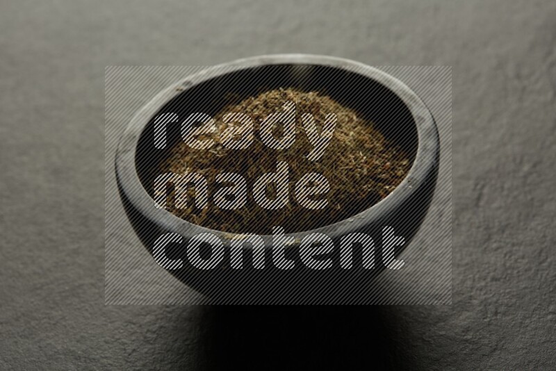 black pottery round sauce bowl filled with herbs on grey textured countertop