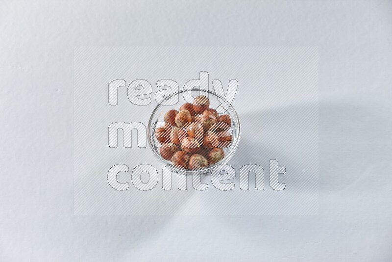 A glass bowl full of hazelnuts on a white background in different angles