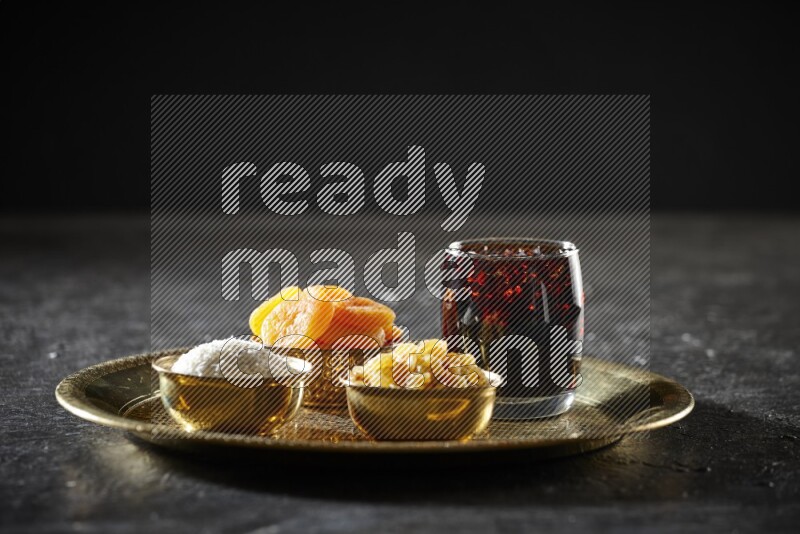 Dried fruits in metal bowls with tamarind on a tray in dark setup