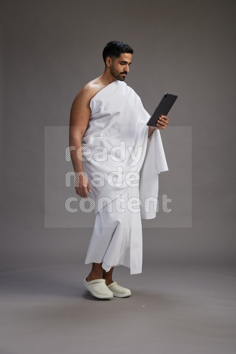 A man wearing Ehram and holding a tablet on gray background
