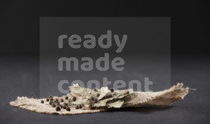 أوراق الغار المجففة مع حبوب البهار الحلو علي قطعة من قماش الخيش علي خلفية سوداء