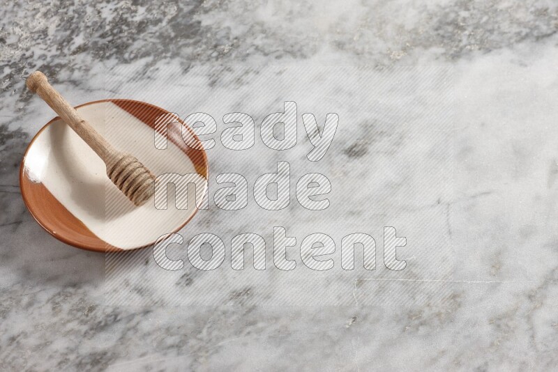 Multicolored pottery plate with wooden honey dipper in it on grey marble background