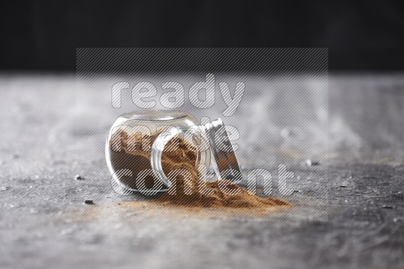 Flipped herbal glass jar full of cinnamon powder on textured black background