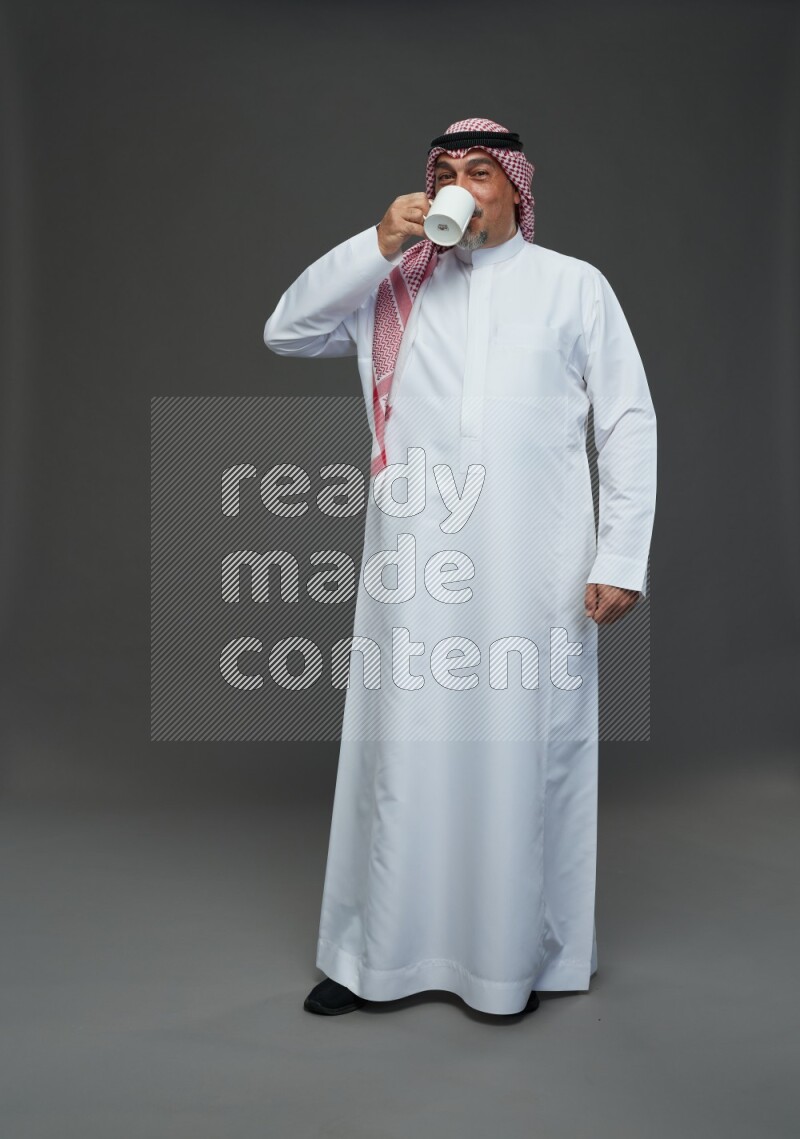 Saudi man with shomag Standing holding mug on gray background