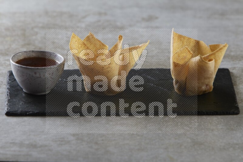 wonton cups with soy sauce ramkin on rectangle slate on grey textured counter top