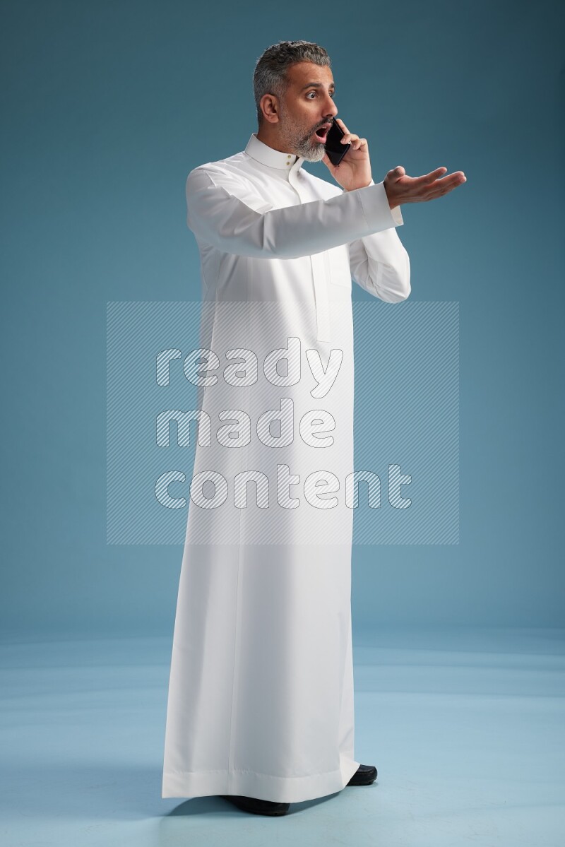 Saudi man wearing thob talking on the phone on blue background