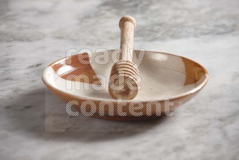 Multicolored pottery plate with wooden honey dipper in it on grey marble background