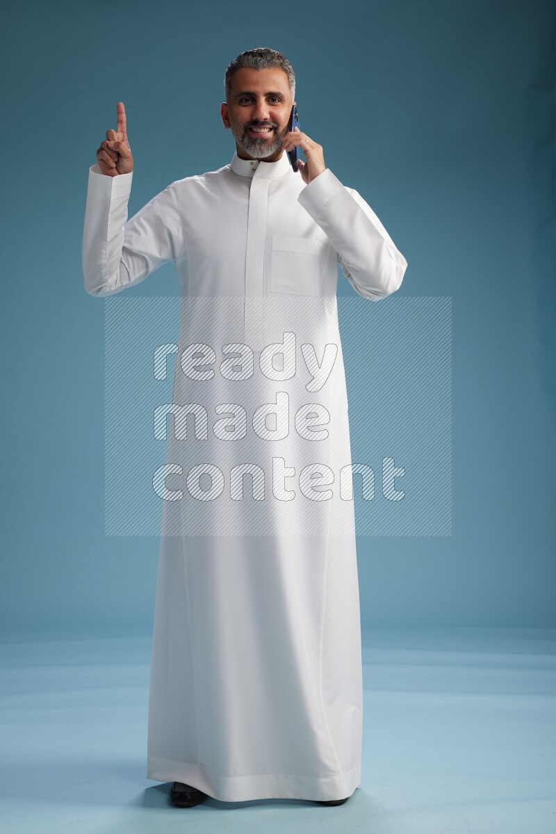 Saudi man wearing thob talking on the phone on blue background