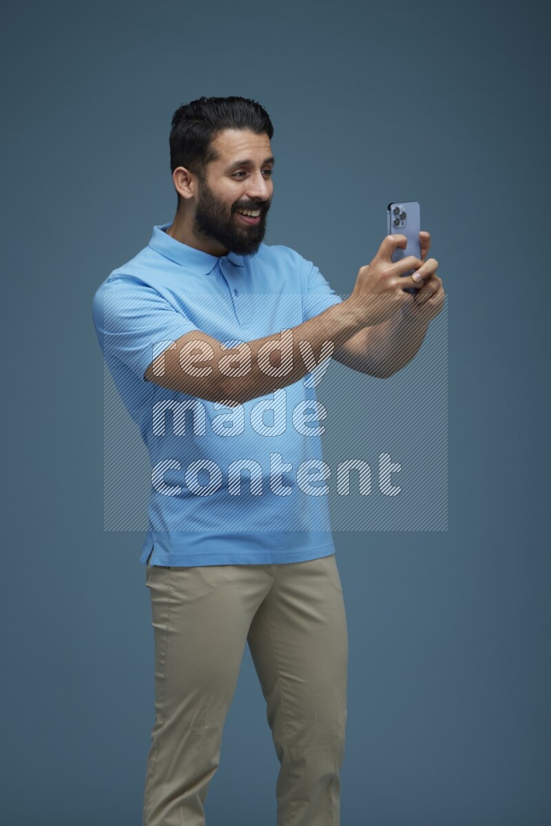 Man taking a picture with his phone  in a blue background wearing a Blue shirt