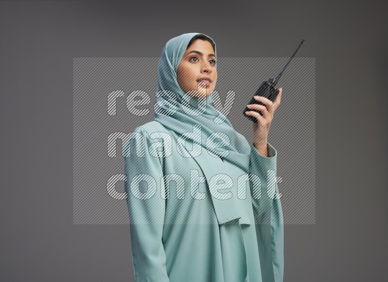 Saudi Woman wearing Abaya standing holding walkie-talkie on Gray background