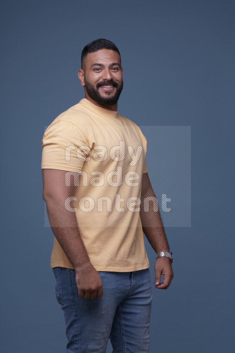 A man posing in a blue background wearing a yellow shirt