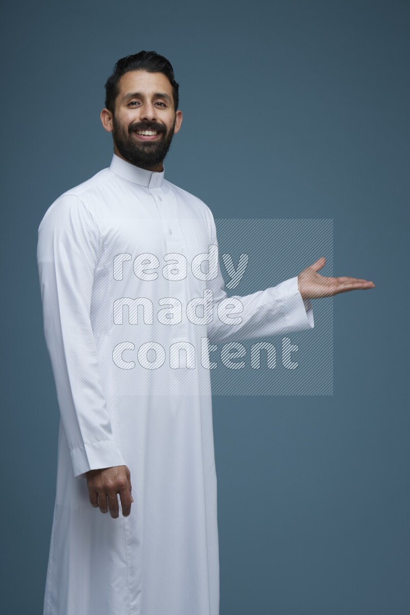 A man pointing in a blue background wearing Saudi Thob