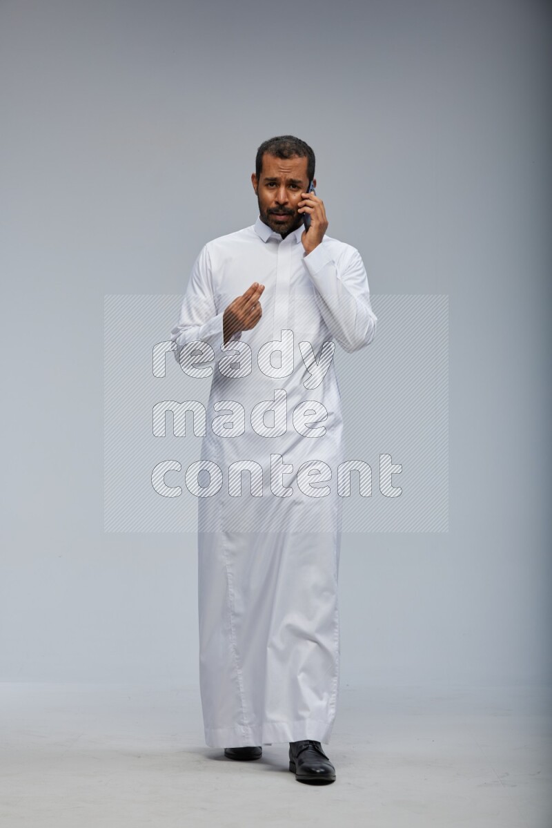 Saudi man wearing Thob standing talking on phone on Gray background