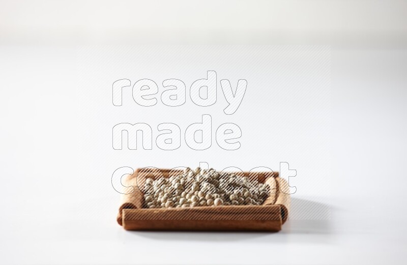 A single square of cinnamon sticks full of white pepper on white flooring