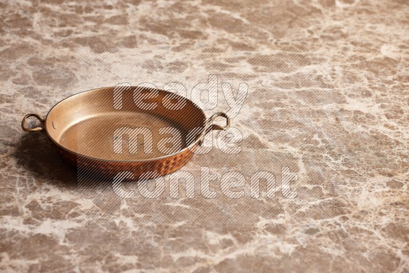 A small copper pan on beige marble background