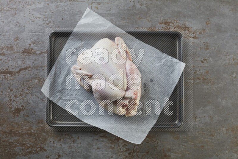 whole raw chicken on an oven trey direct on a rustic grey background