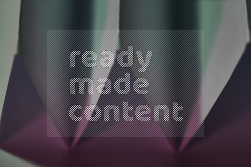 A close-up abstract image showing sharp geometric paper folds in green and pink gradients