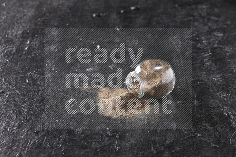 بودرة الفلفل الأسود في وعاء زجاجي مقلوب علي خلفية سوداء