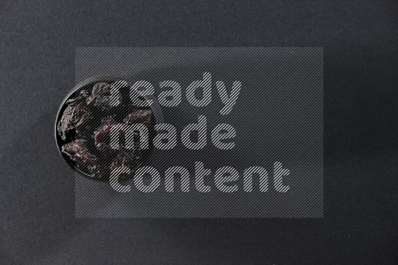 وعاء فخاري أسود ممتلئ بالبرقوق المجفف على خلفية سوداء