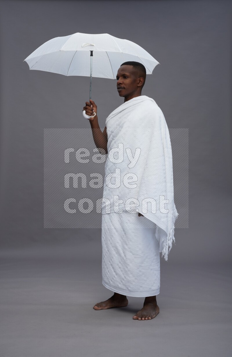 A man wearing Ehram Standing holding umbrella on gray background