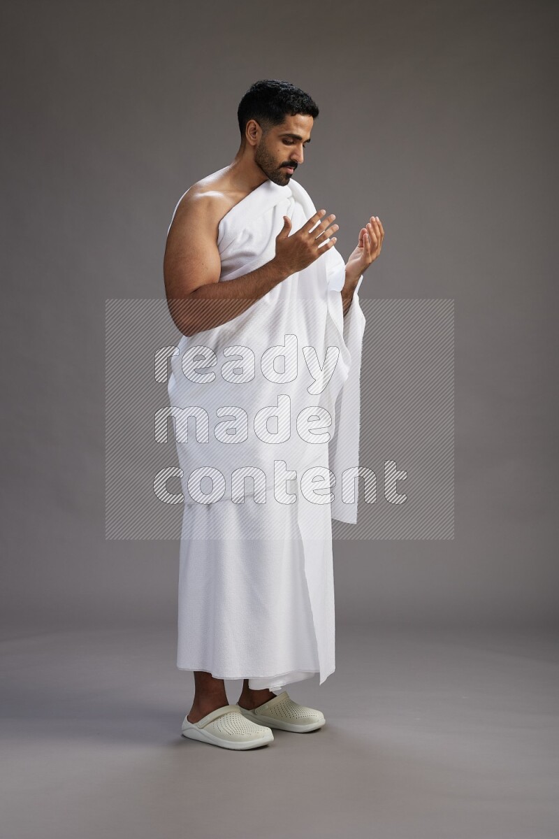 A man wearing Ehram Standing performing dua'a on gray background