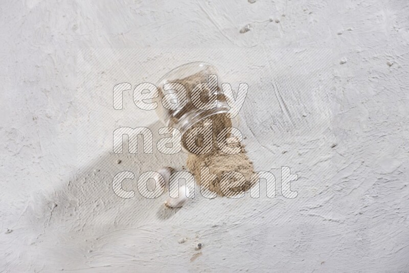 A glass jar full of garlic powder flipped over with the powder came out on a textured white flooring