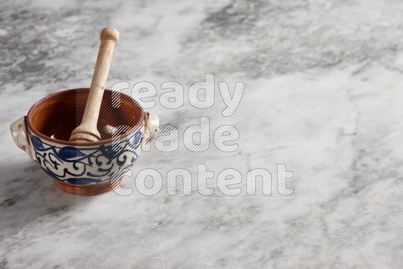 Decorative pottery pot with wooden honey dipper in it on grey marble background