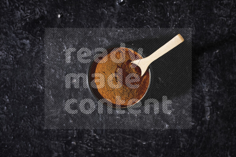 A black pottery bowl full of ground paprika powder on black background