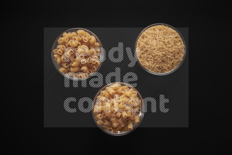 Different pasta types in glass bowls on black background