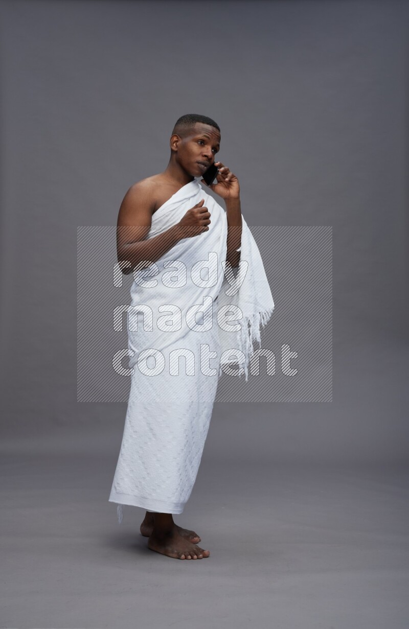 A man wearing Ehram Standing talking on phone on gray background