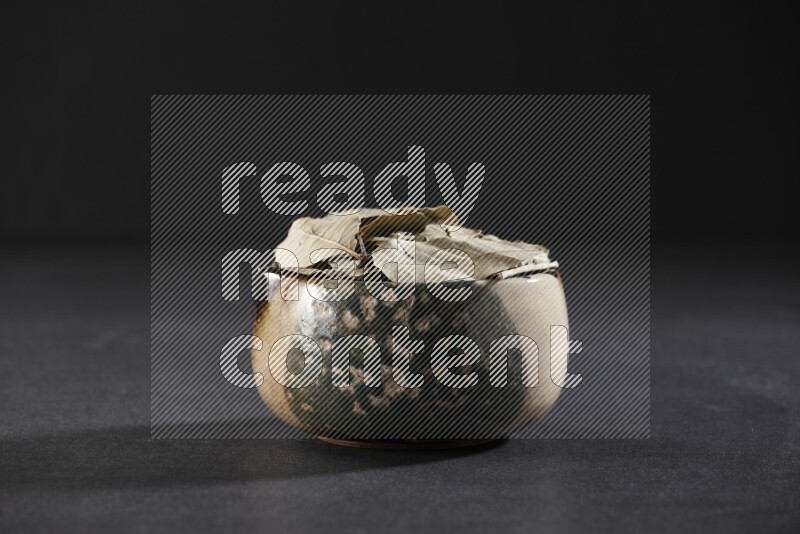 A multicolored pottery bowl full of dried bay leaves on black flooring