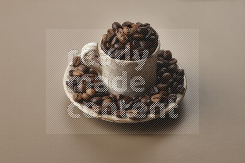 A beige pottery cup full of roasted coffee beans on beige background