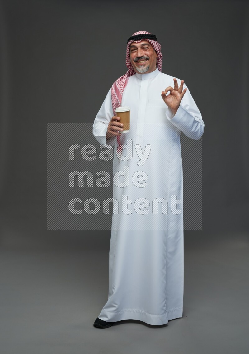 Saudi man with shomag Standing holding paper cup on gray background