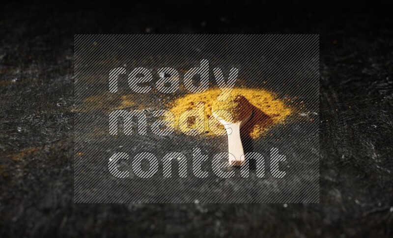 A wooden spoon full of turmeric powder on textured black background