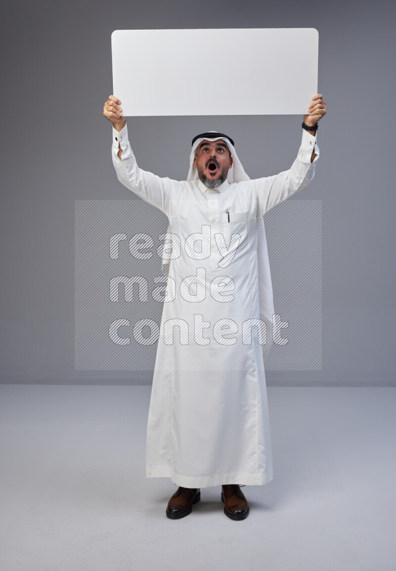 Saudi man Wearing Thob and white Shomag standing holding board on Gray background