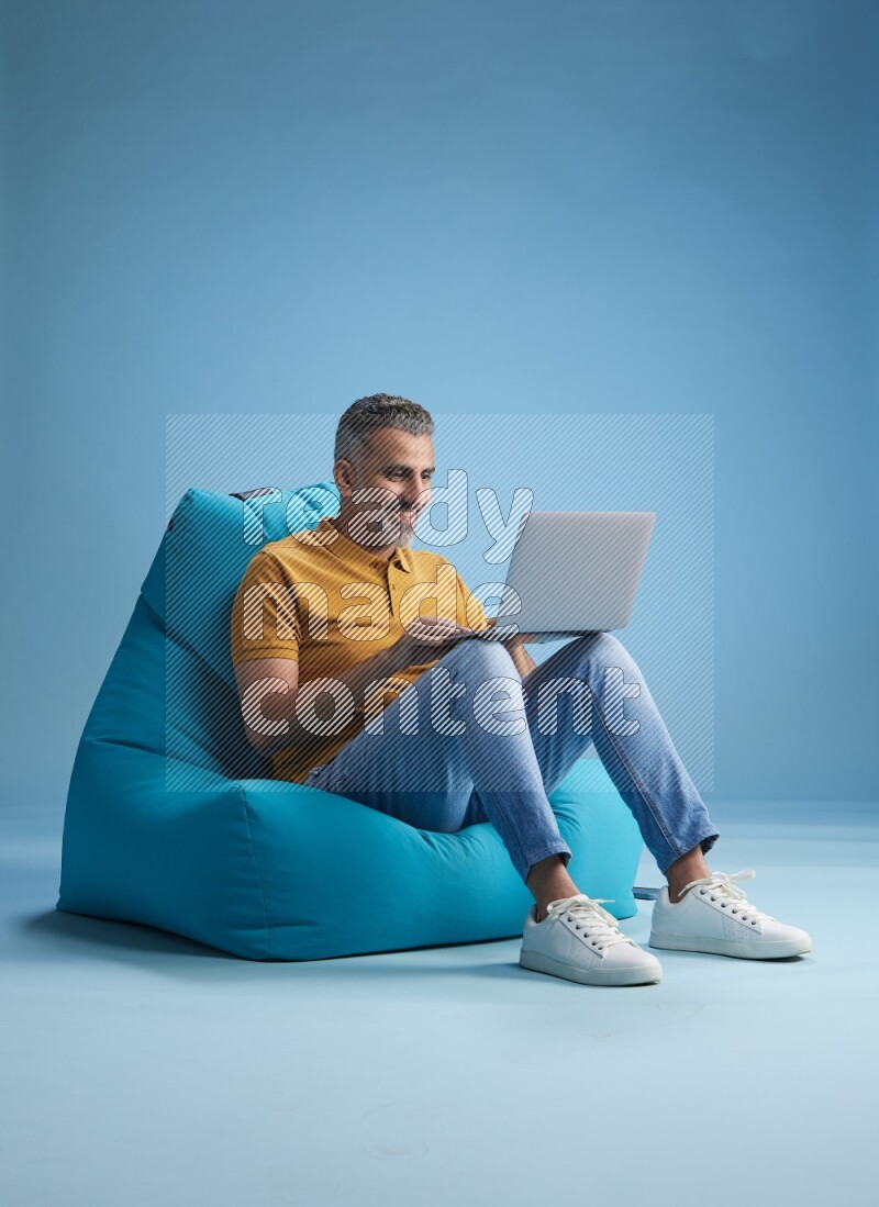 A man sitting on a blue beanbag and working on laptop