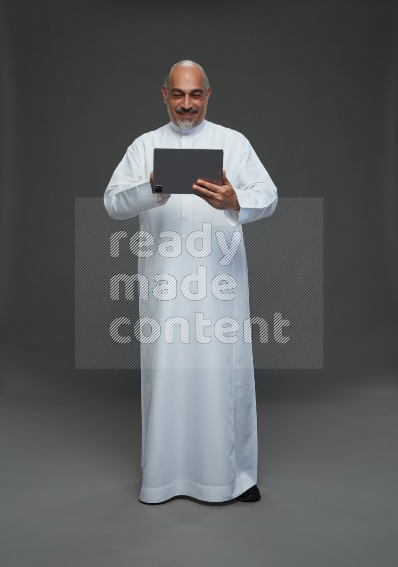 Saudi man without shomag Standing working on tablet on gray background