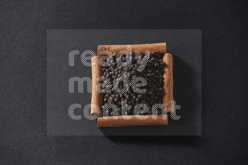 A single square of cinnamon sticks full of black pepper on black flooring