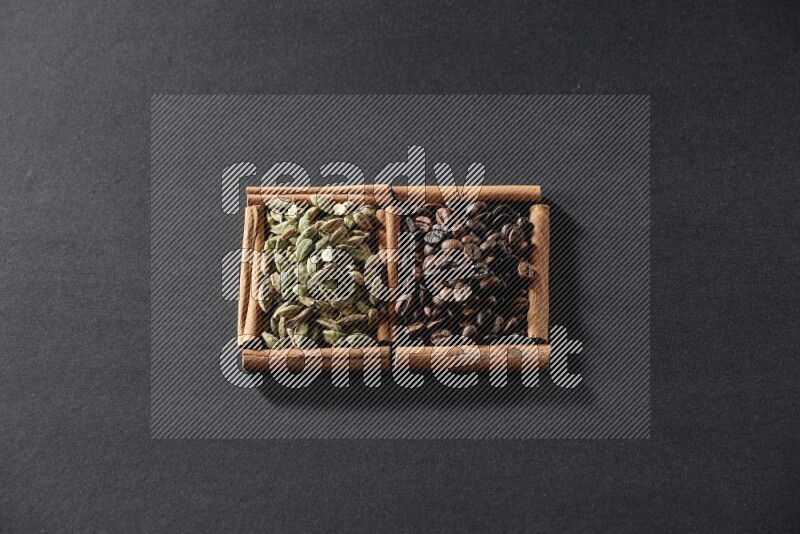 مربعان من أعواد القرفة ممتلئان بحبوب القهوة وحبوب الهيل علي خلفية سوداء