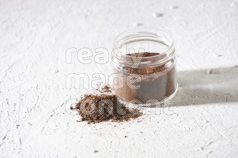 A glass jar full of cloves powder on a textured white flooring