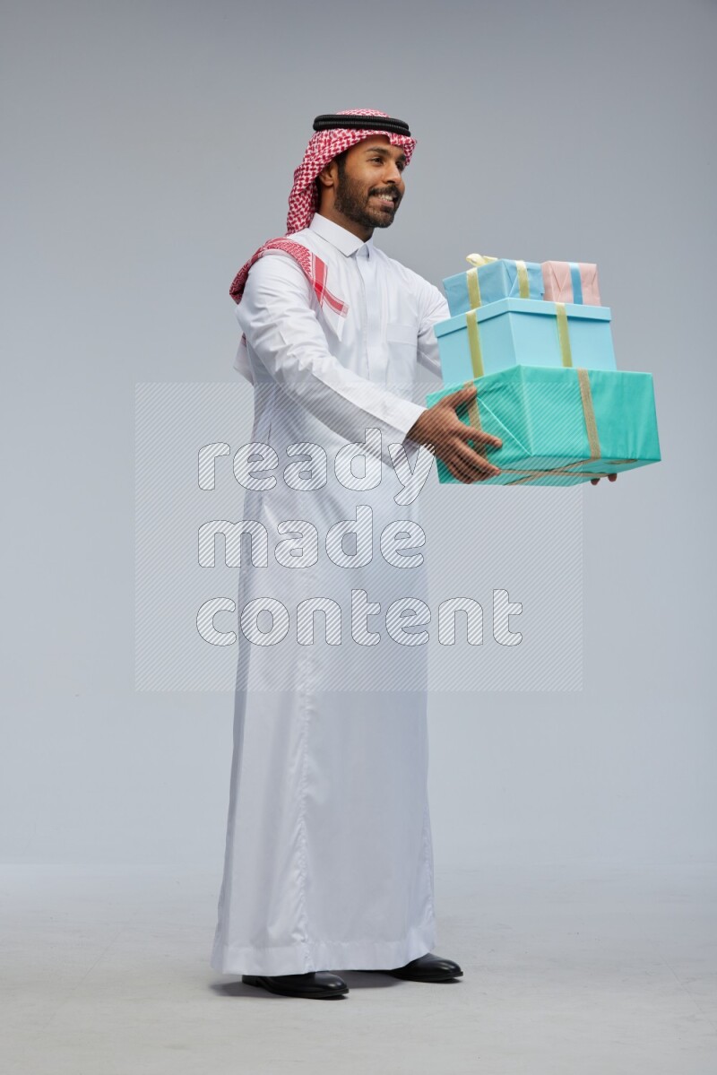 Saudi man Wearing Thob and shomag standing holding gift box on Gray background