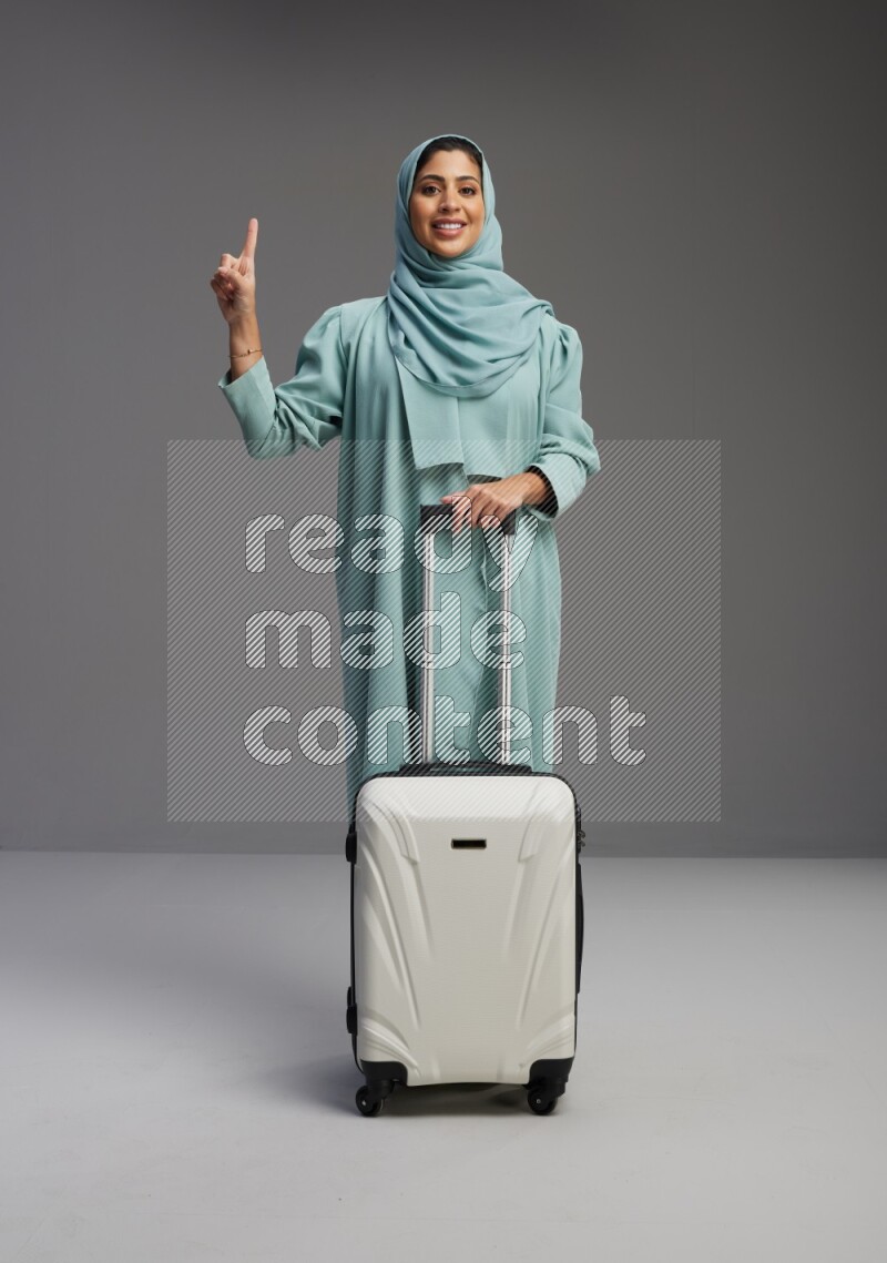 Saudi Woman wearing Abaya standing holding Travel bag on Gray background
