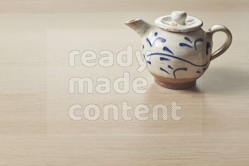 A pottery teapot on light wooden background