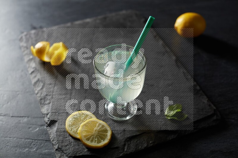 A glass of lemon juice with a straw on black background