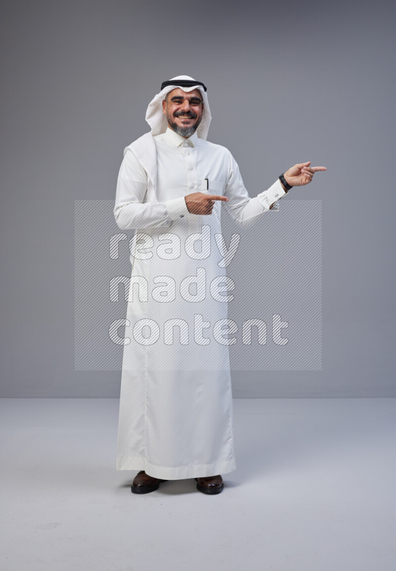 Saudi man Wearing Thob and white Shomag standing interacting with the camera on Gray background