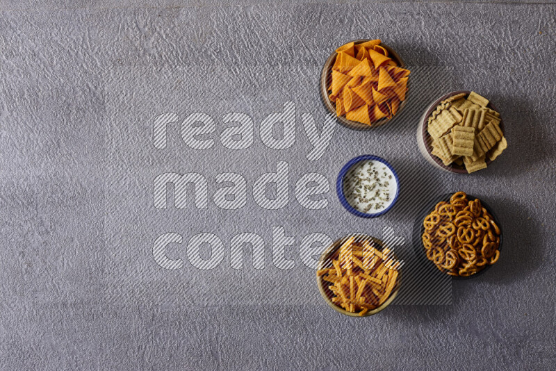 Assorted snacks in pottery bowls on grey background